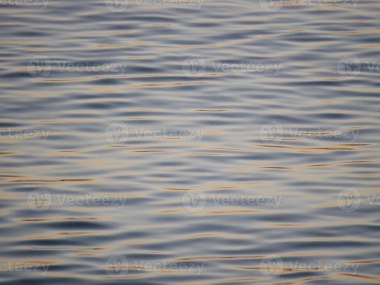 A tranquil close-up of gently rippling water illuminated by warm, golden light from a sunset. Wave pattern for wellness, nature, or background theme concepts photo