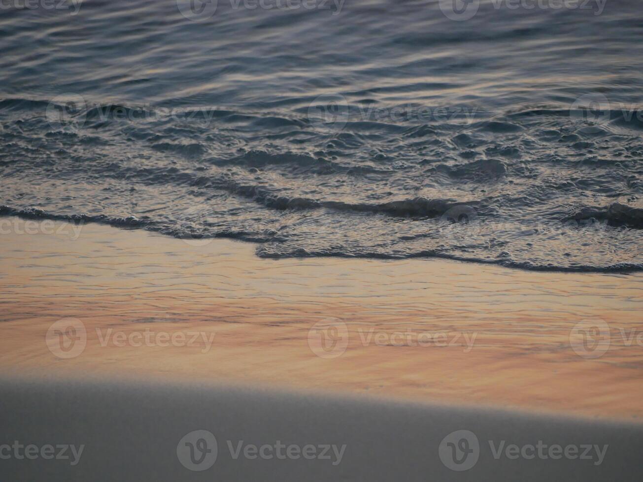 Gentle ocean waves lapping against the shore with wet sand. A serene coastal scene during golden hour. Background theme related to relaxation, mindfulness, travel, nature, and wellness photo