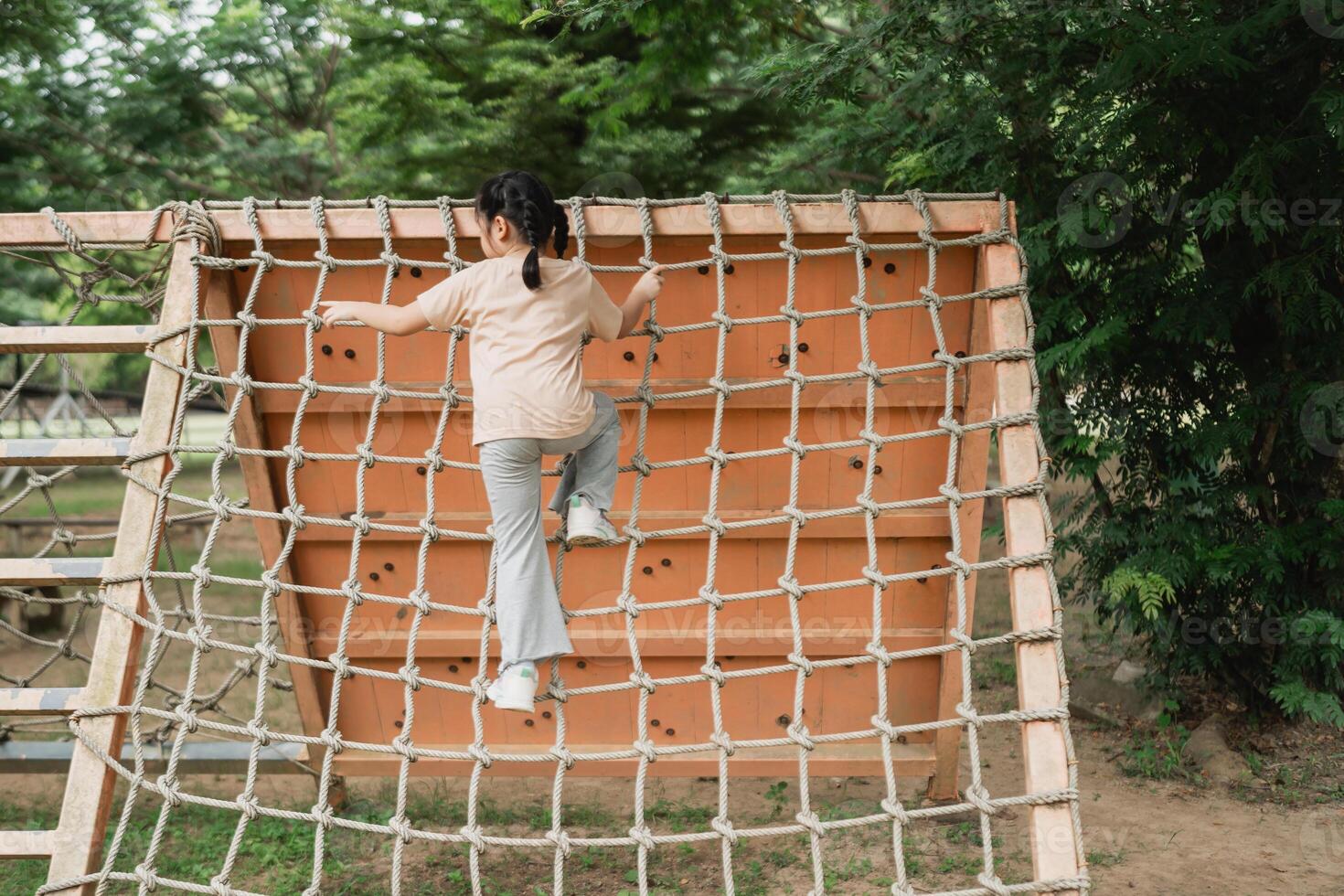 Child Climbing a Vertical Playground Net in a Park Surrounded by Lush Green Trees on a Sunny Day, Joyful Outdoor Activity for Kids photo