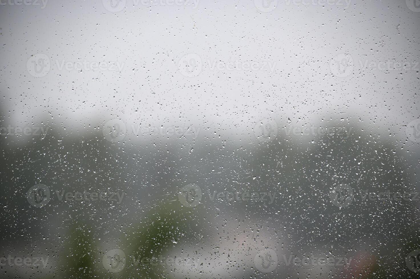 Raindrops on a window obscure the tranquil view of a misty landscape. photo