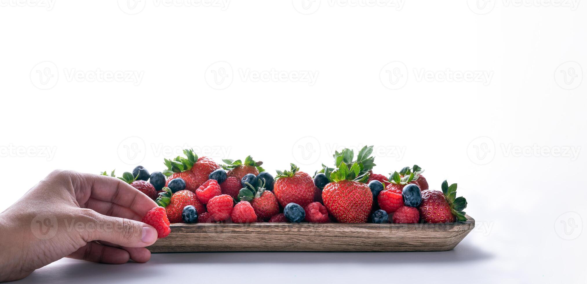 Human hand taking fresh berries over a wood plate isolated on white background. photo
