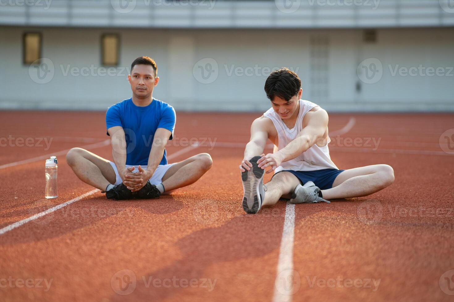 Two asian athlete men stretching their foots together, sitting on the racetrack in sports stadium. photo