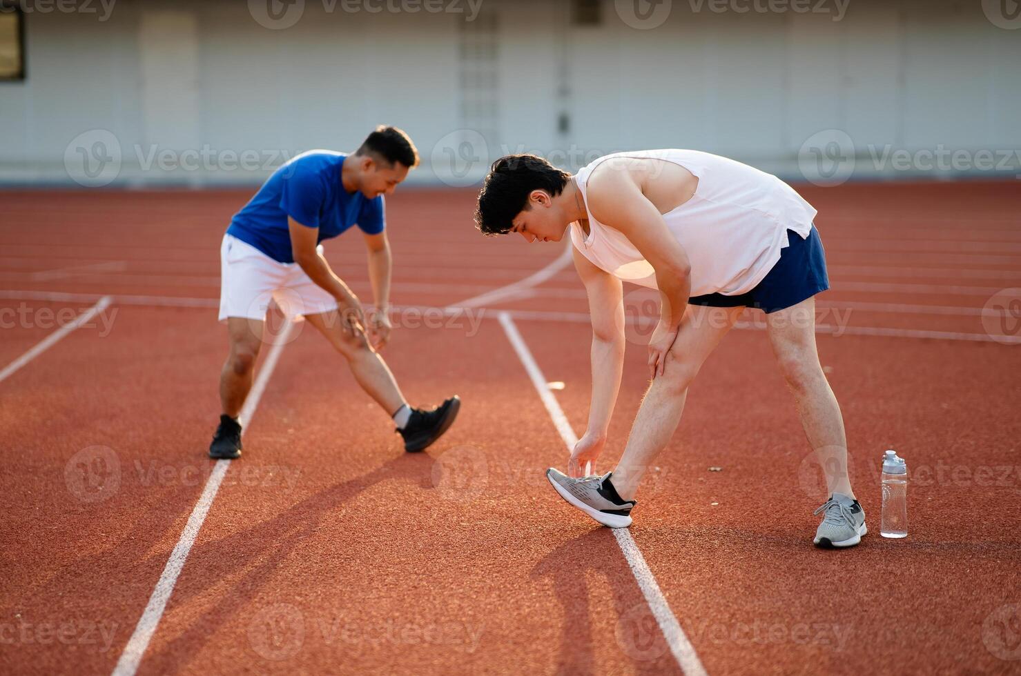Two asian athlete men are stretching their legs and foots together on the racetrack in sports stadium. photo