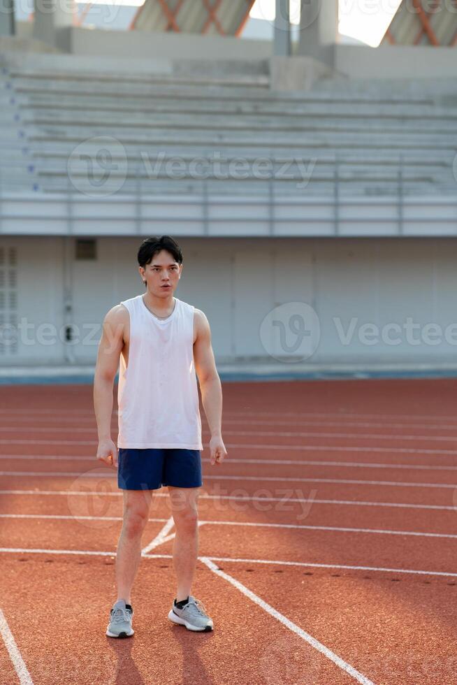 An asian man in white tank top is standing and looking ahead while taking a rest after running. photo