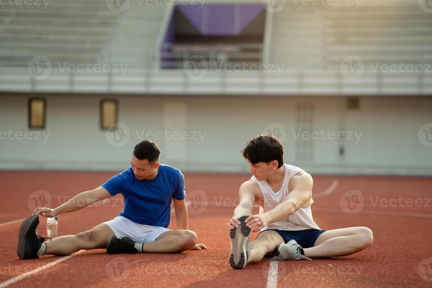 Two asian athlete men sitting and stretching their foot together on the racetrack in sports stadium. photo