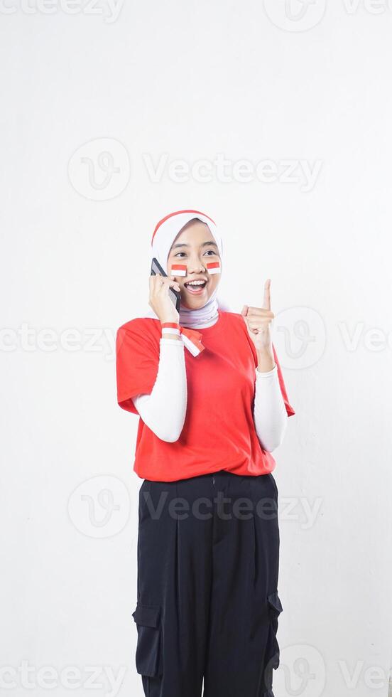 Indonesia independence day celebration concept with happy Asian girl wearing red and white Indonesia flag color attribute talking on the phone call isolated on white background photo