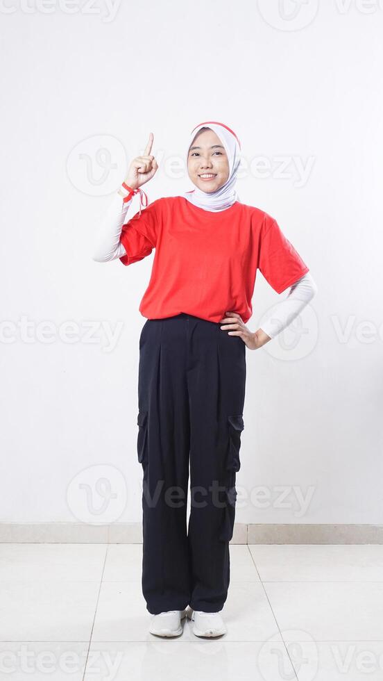 Beautiful Asian girl celebrate Indonesia independence day with red and white outfit raising her index finger to the up isolated on white background photo