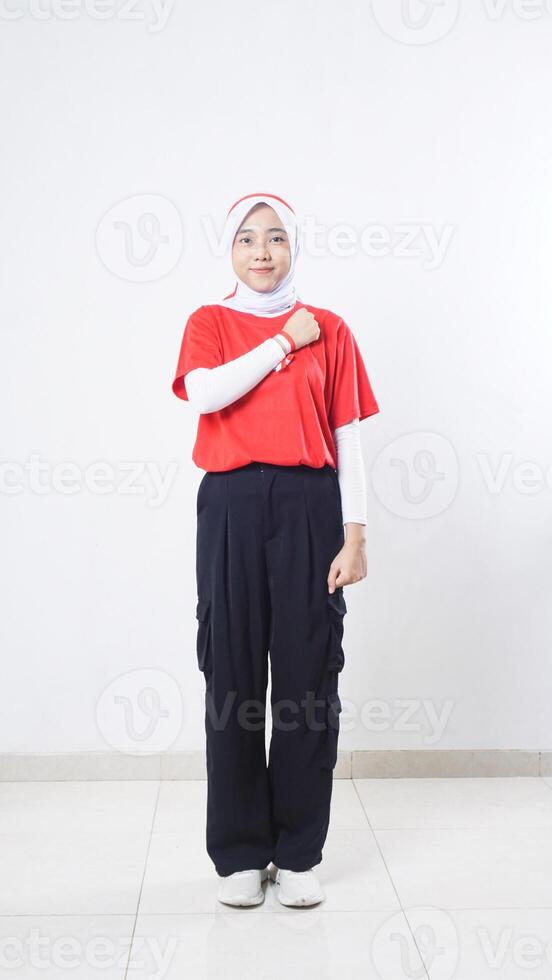 Asian girl celebrate Indonesia independence day with red and white outfit showing salute pose with putting her clenched fist over the heart isolated on white background photo