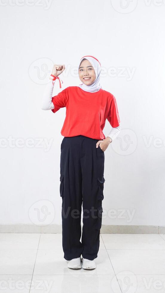 Beautiful Asian girl celebrate Indonesia independence day with red and white outfit showing winning gesture with raising her clenched fist isolated on white background photo