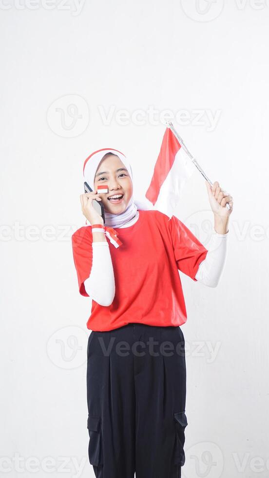 Indonesia independence day celebration concept with excited Asian girl wearing red and white Indonesia flag color attribute talking on the phone call isolated on white background photo