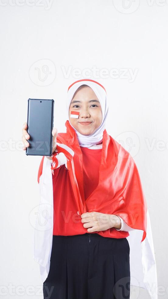 Indonesia independence day celebration with Asian girl wearing red and white Indonesia flag color attribute showing blank screen smartphone to camera isolated on white background photo
