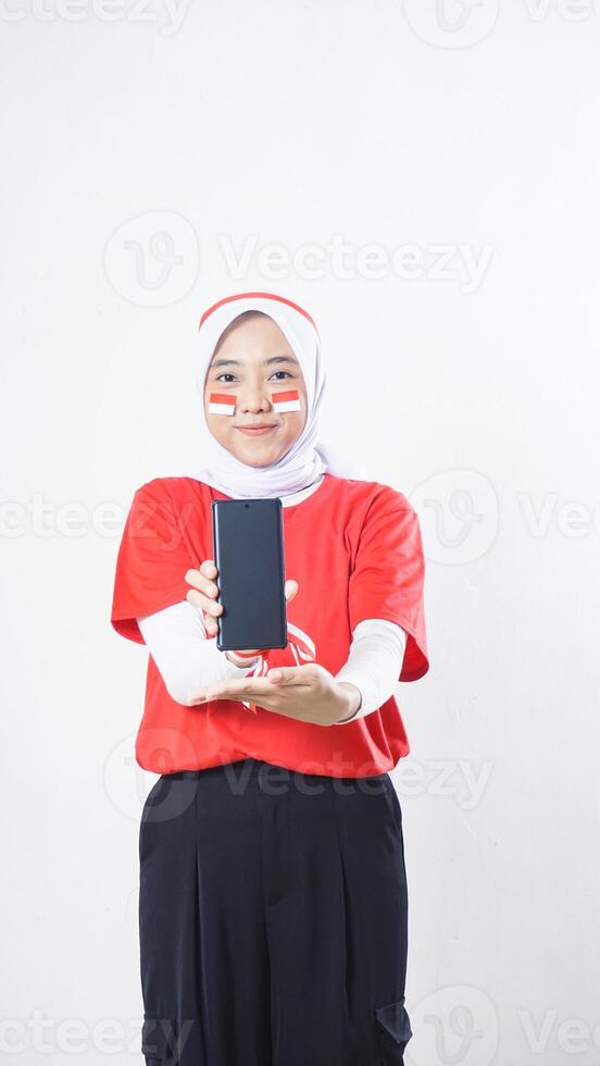 Indonesia independence day celebration with Asian girl wearing red and white Indonesia flag color attribute showing smartphone blank screen to camera isolated on white background photo