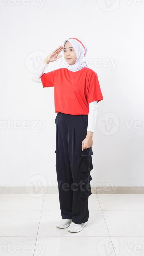 Side view of Asian girl celebrate Indonesia independence day with red and white outfit showing salute pose with raising her right hand to the eyebrow isolated on white background photo
