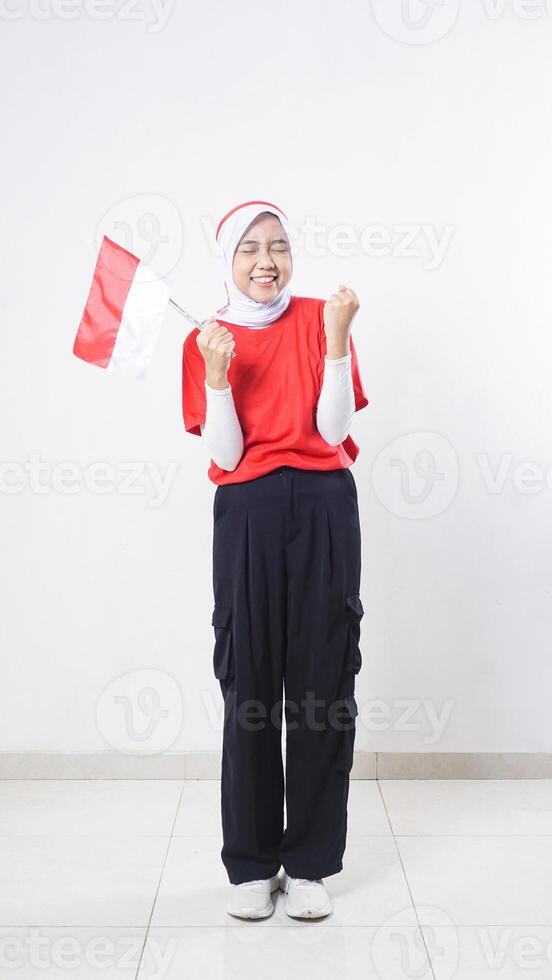 Indonesia independence day celebration with beautiful Asian girl wearing red and white outfit showing celebration pose while holding mini Indonesia flag decoration isolated on white background photo