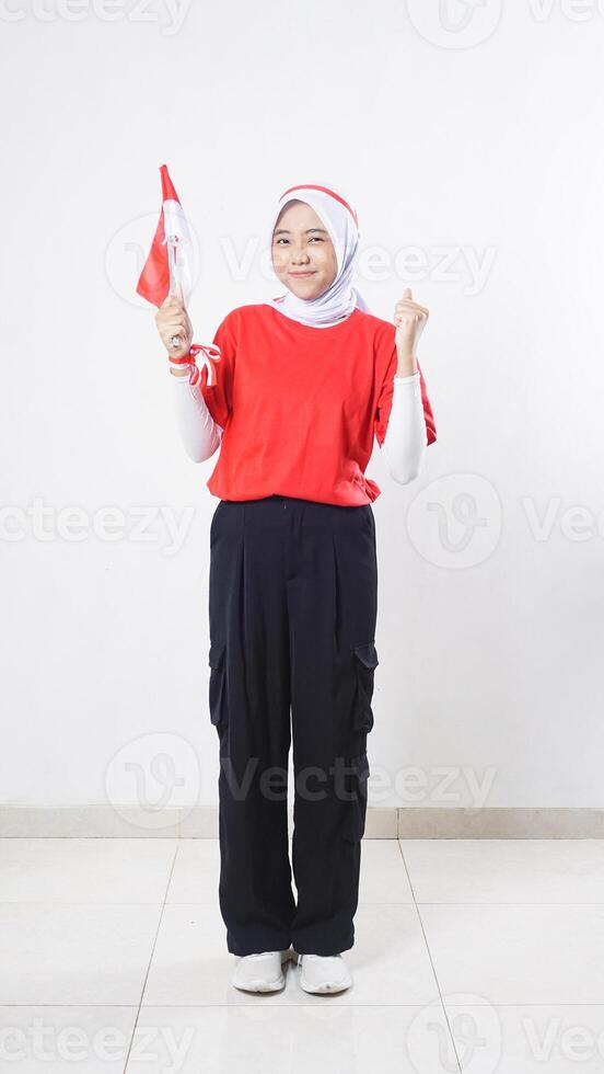 Indonesia independence day celebration with Asian girl wearing red and white outfit holding mini Indonesia flag decoration and doing celebration pose with hand clenched isolated on white background photo