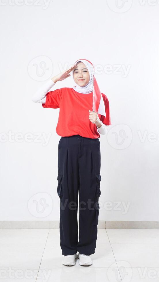 Indonesia independence day celebration with beautiful Asian girl wearing red and white outfit holding mini Indonesia flag decoration and doing salute pose isolated on white background photo