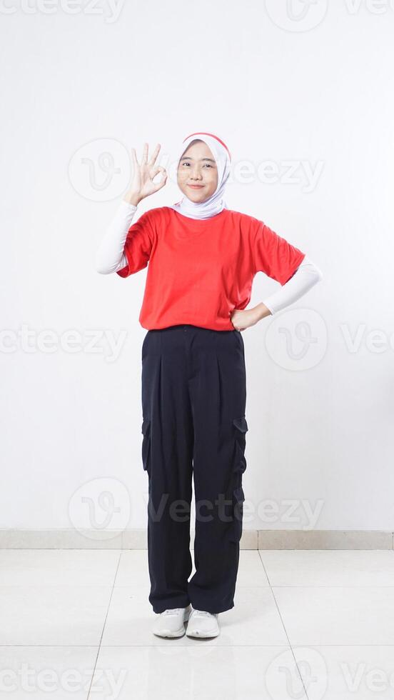 Asian girl celebrate Indonesia independence day with red and white outfit showing OK sign hand gesture isolated on white background photo