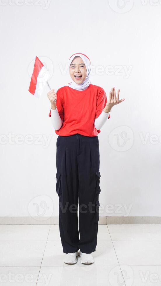 Indonesia independence day celebration with excited Asian girl wearing red and white outfit holding mini Indonesia flag decoration isolated on white background photo