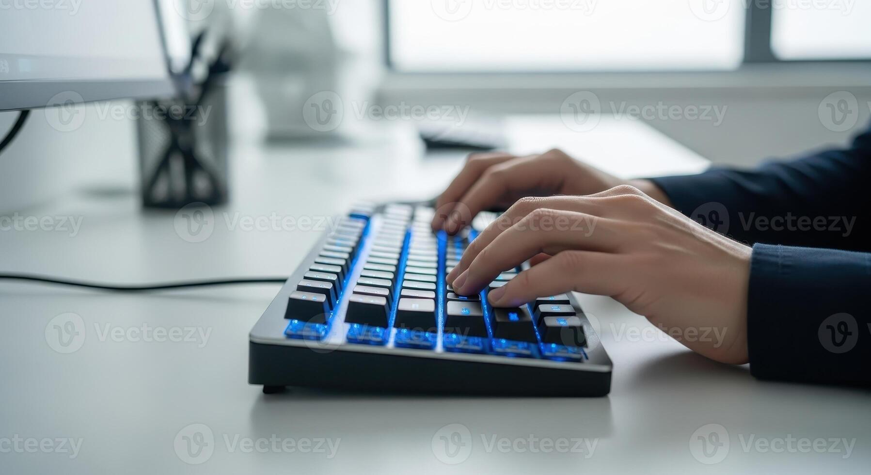 Hands typing on a blue backlit computer keyboard at desk photo