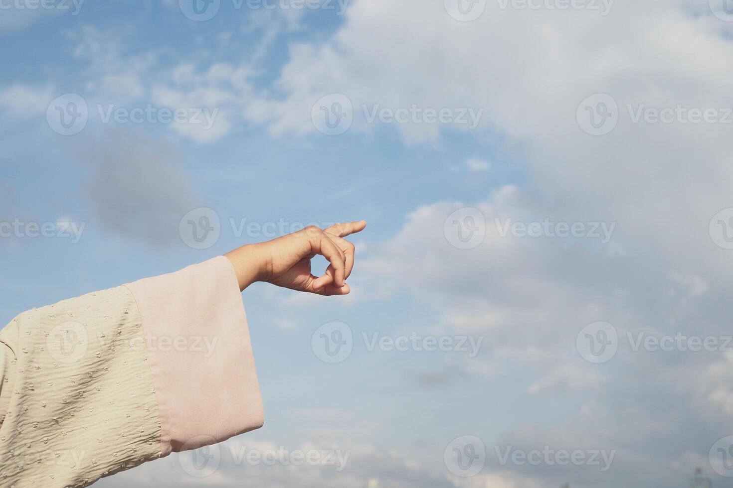 Hand reaching towards a bright blue sky with clouds photo