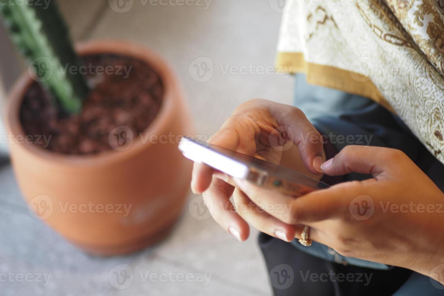 Woman using smartphone while seated near potted plant photo