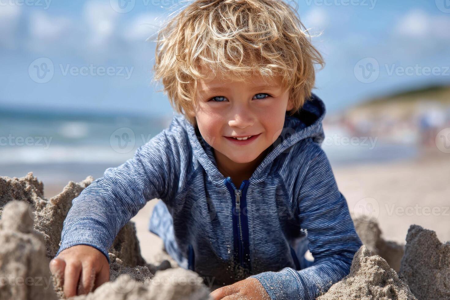 Boy builds sandcastle on sunny beach with clear sky and gentle w photo