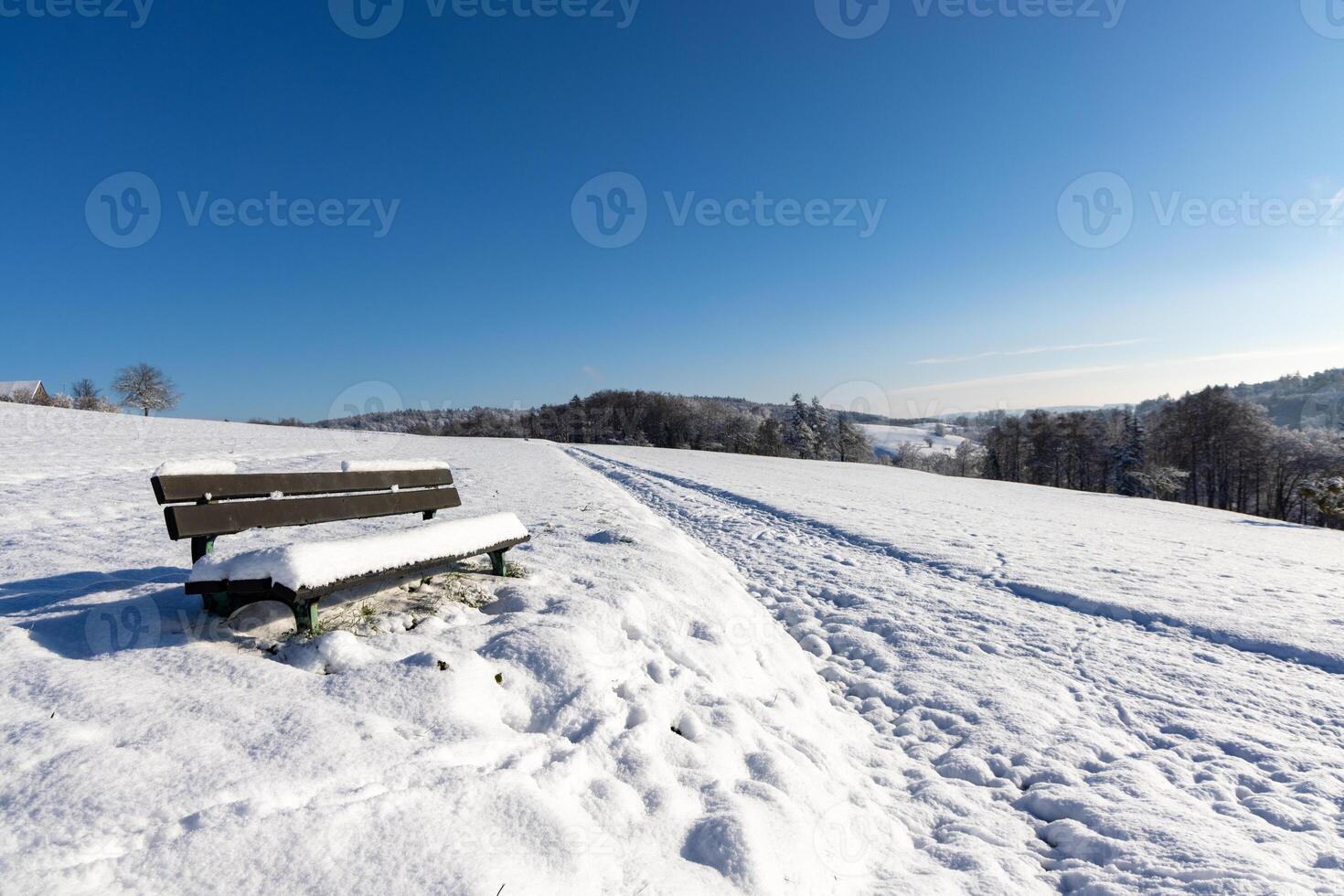 Empty bench covered in snow in a field on a clear winter sunny daySnowcovered empty bench in sunny winter field photo