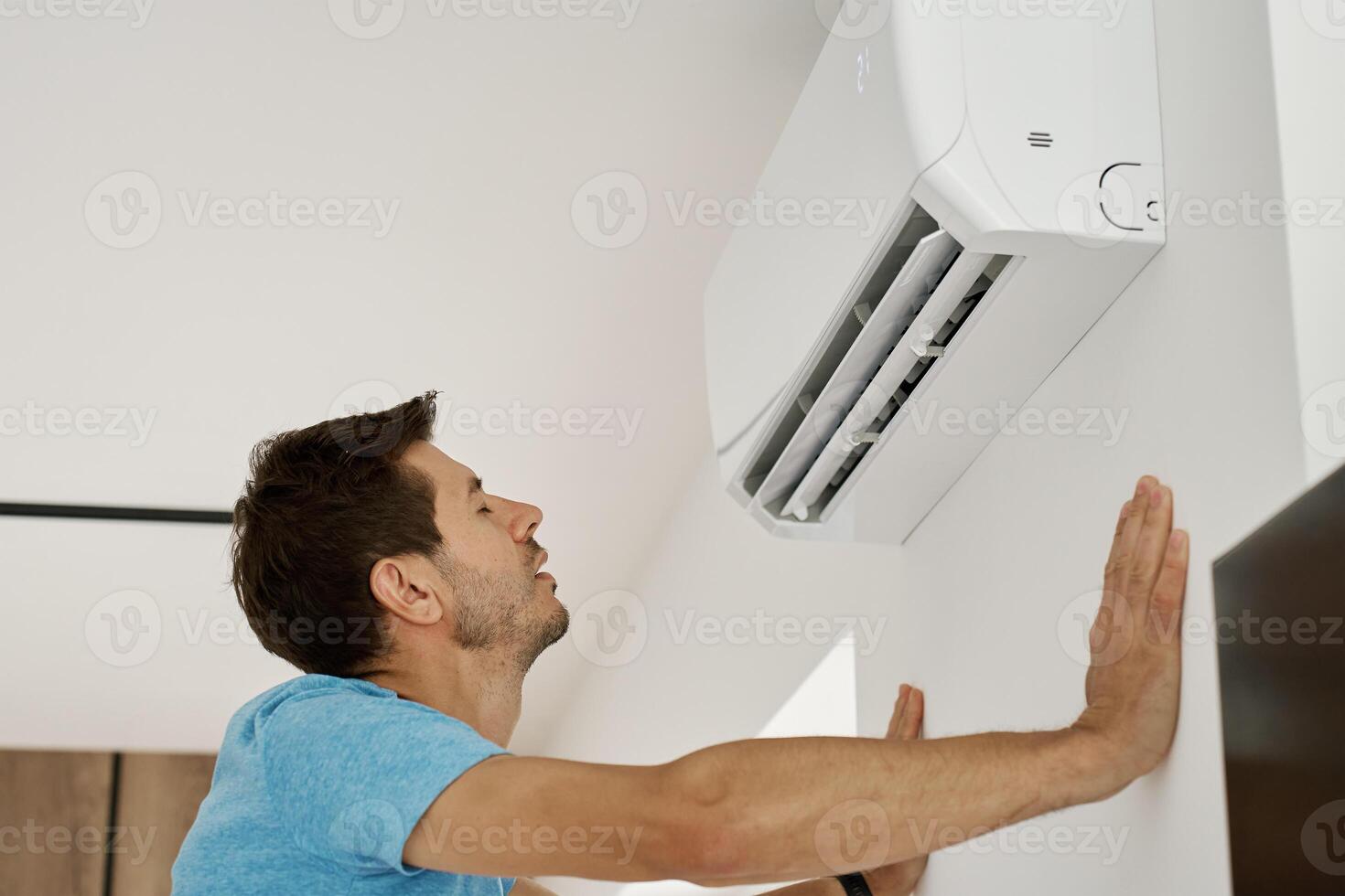 Man enjoying cool air from wall mounted air conditioner photo