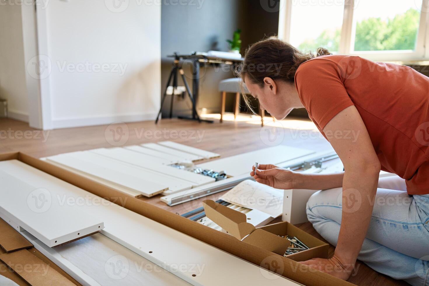 Woman assembling furniture parts at home with instruction manual photo