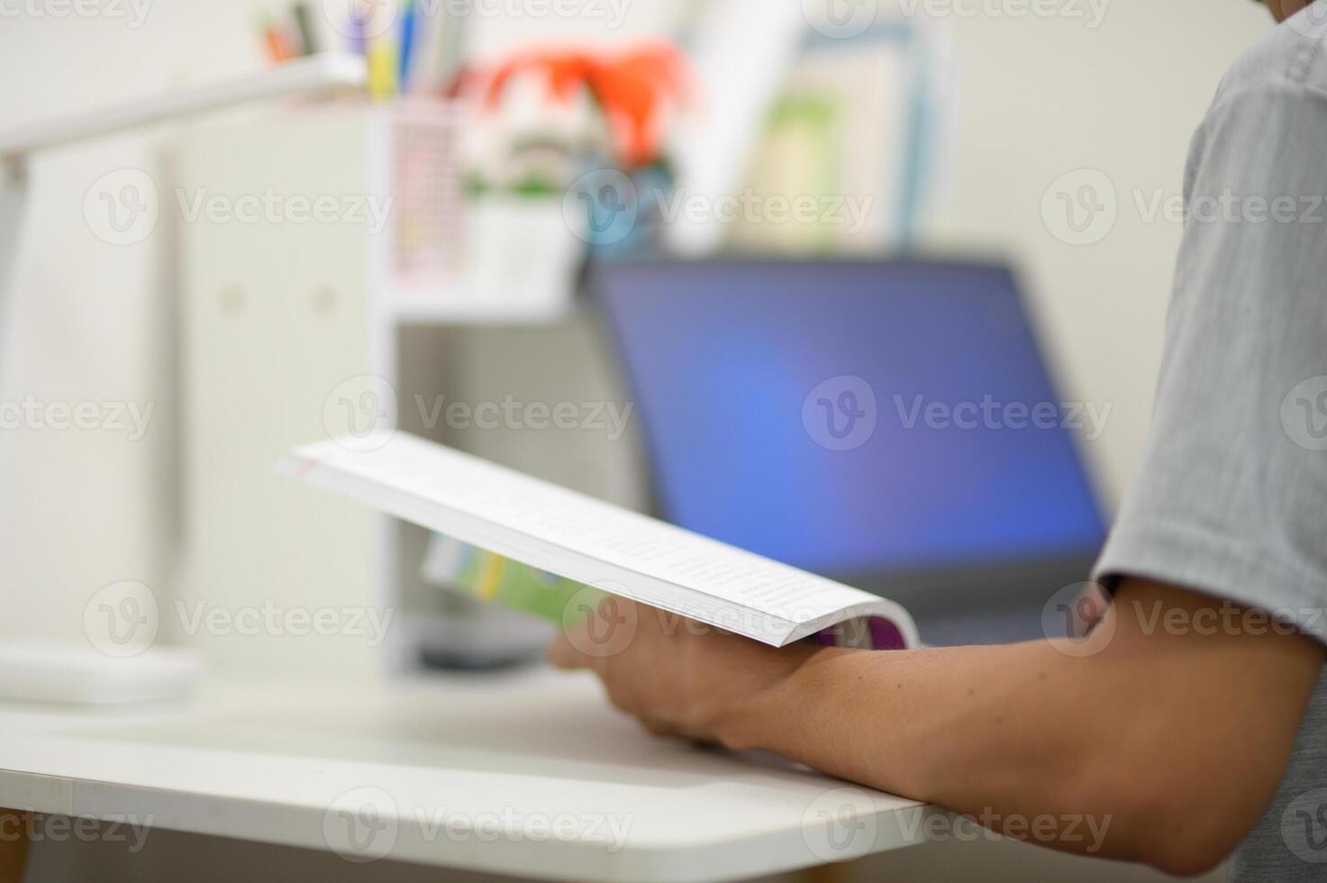Person Holding Book in Modern Workspace with Laptop on Desk photo