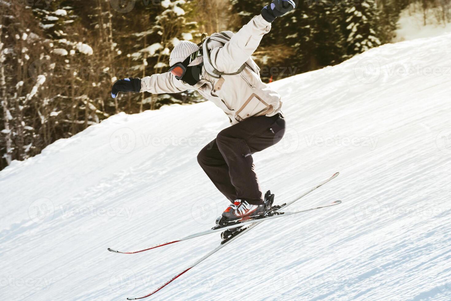 Young male skier training in white jacket black pants jumps off freestyle on snowy slope mid-air trick forest winter freestyle ride extreme sport concept photo