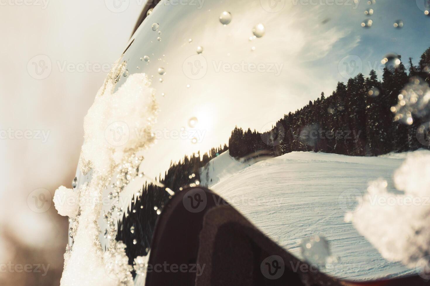 Macro view ski resort reflected in ski goggles with water drops, pine forest under clear winter sky, concept extreme sport, safety, perspective. photo