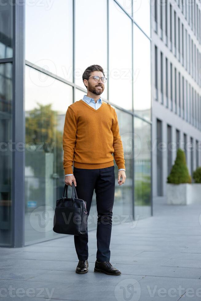 A businessman stands confidently in front of a modern building, holding a briefcase, looking off into the distance. photo