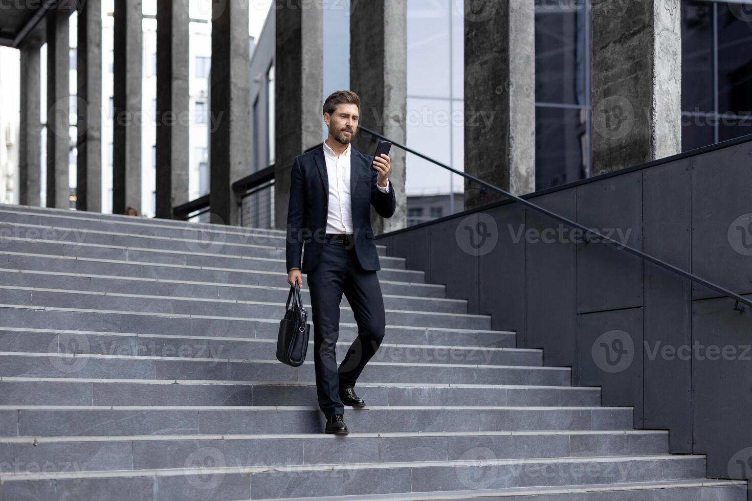 A businessman in a suit descends outdoor stairs while holding a phone and briefcase, modern city backdrop. photo