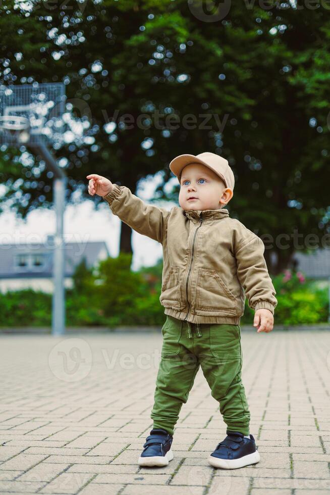 A curious little toddler dressed in trendy and casual outdoor attire joyfully points excitedly at something interesting in a lively park, radiating pure carefree spirit and the wonder of childhood photo