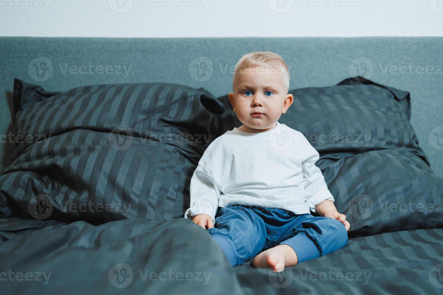 A cheerful toddler sits on a plush bed with colorful pillows, creating a warm atmosphere that radiates joy, innocence, and playful spirit, embodying the essence of childhood and familial love photo