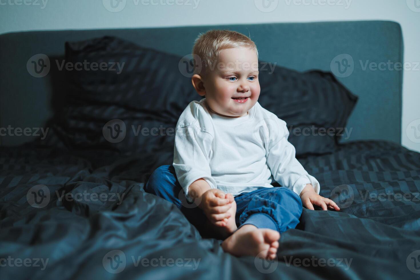 An adorable baby is delightfully sitting on a cozy bed, wearing a joyful expression while surrounded by a bright and cheerful room setting that enhances the overall warm atmosphere of the space photo