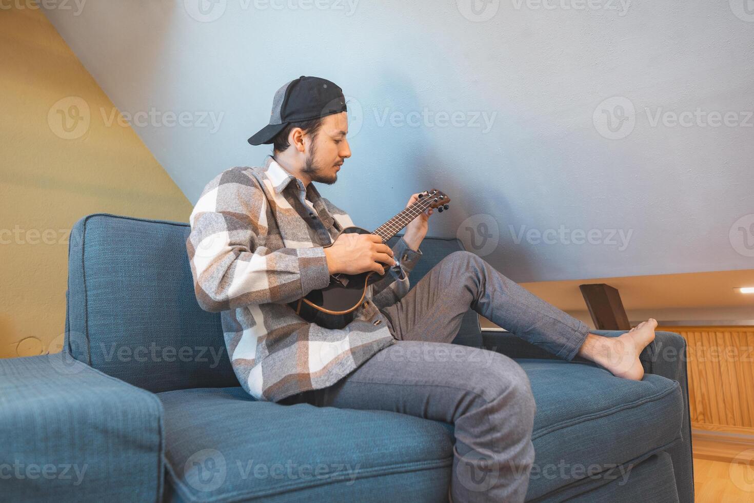 A relaxed boy practices ukulele on a patterned throw in a modern living room photo
