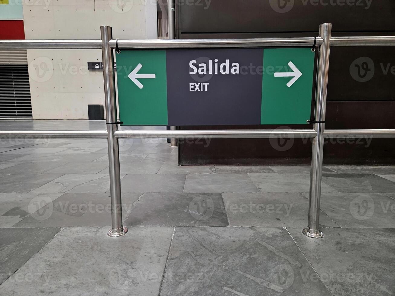 Exit sign with arrows to the right and left and translation into English and Spanish at the station. Emergency exit sign with bilingual directions in modern commercial space photo