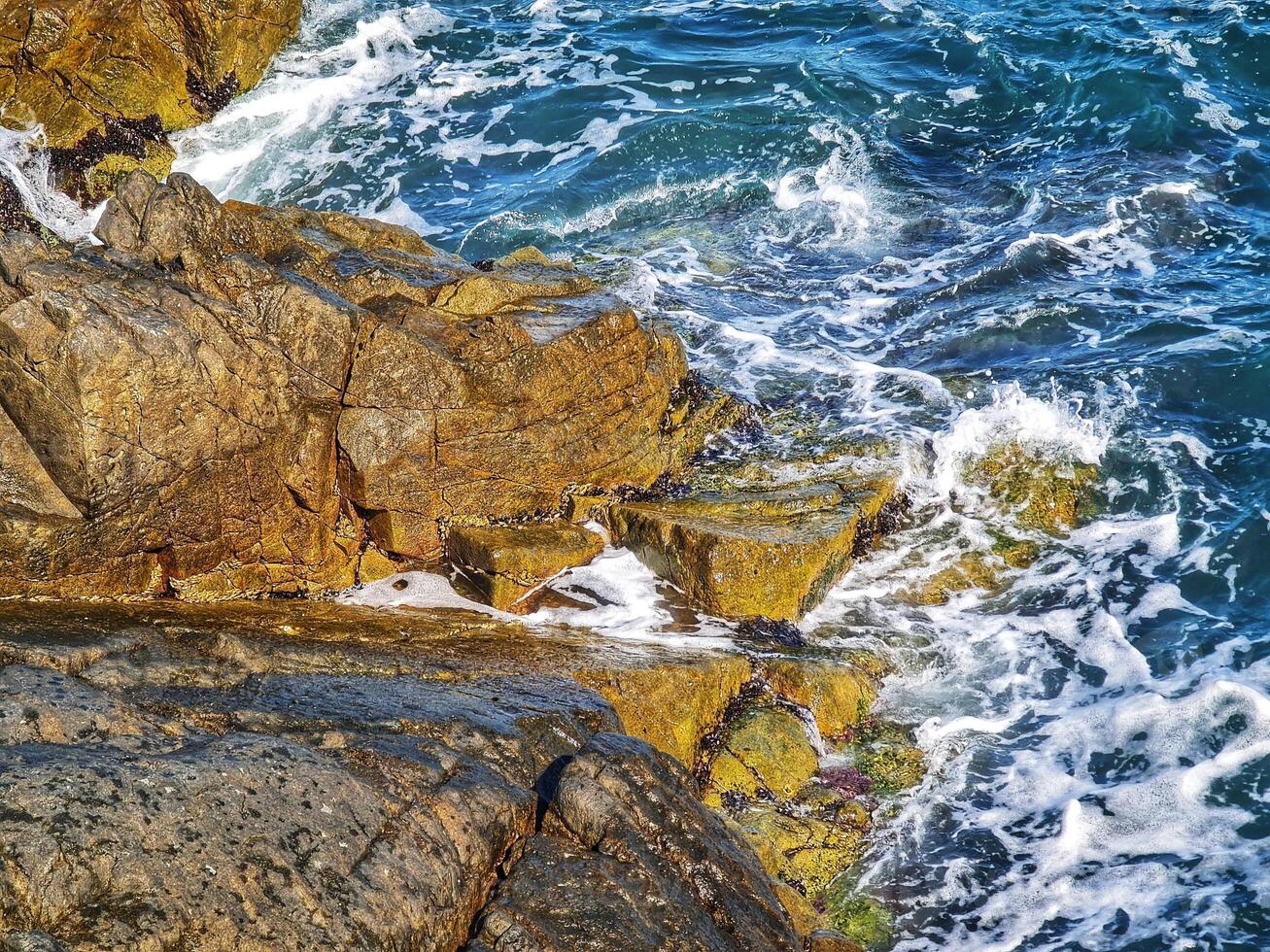 Waves Crashing Onto Rocky Shoreline on Sunny Day photo