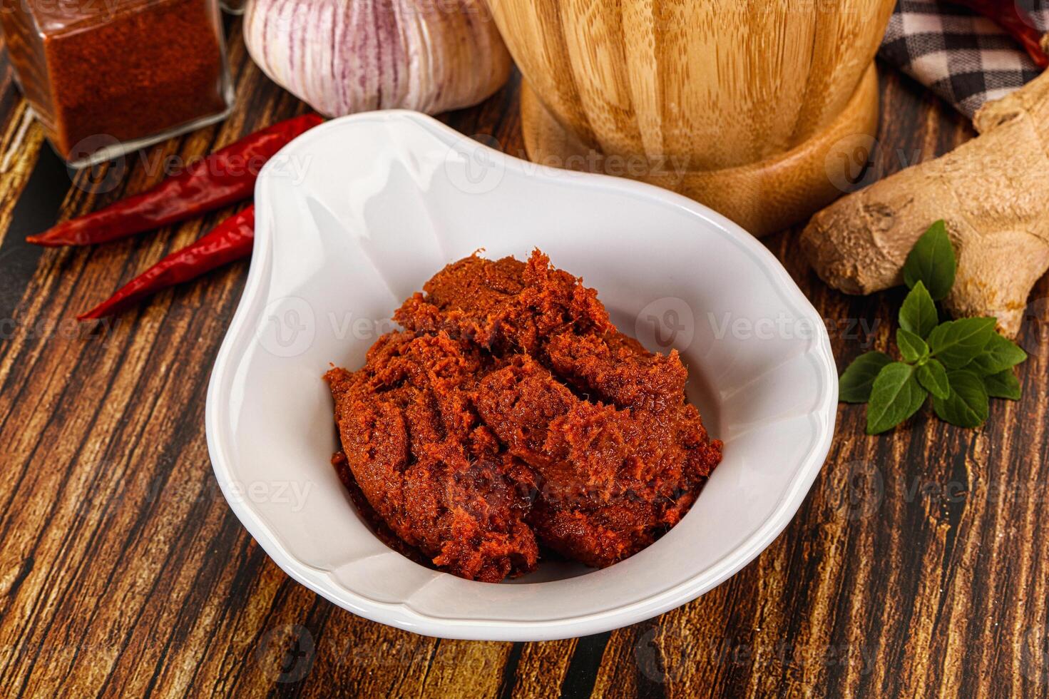 A bowl of red curry with spices and a wooden spoon photo