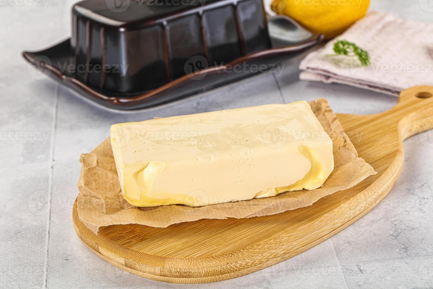 A piece of butter sits on a cutting board next to a lemon photo