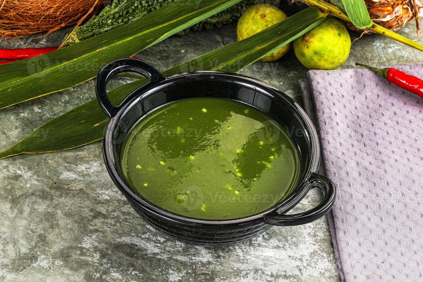 A bowl of green soup with a coconut and some other vegetables photo