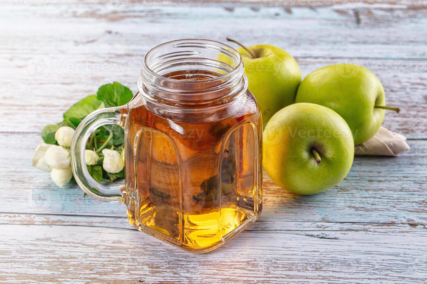 A jar of apple cider and some apples on a wooden table photo