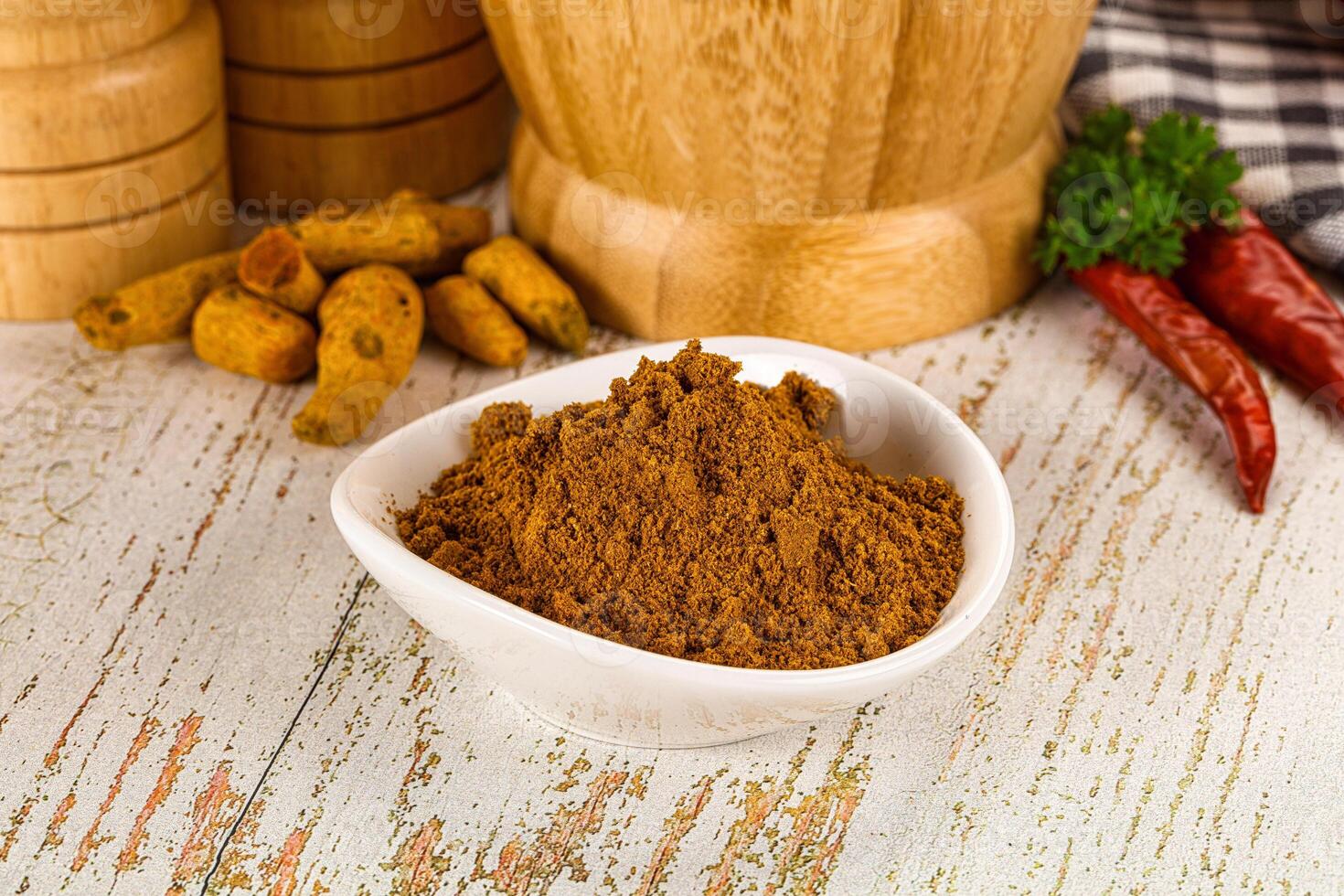 A bowl of curry powder next to a wooden bowl photo