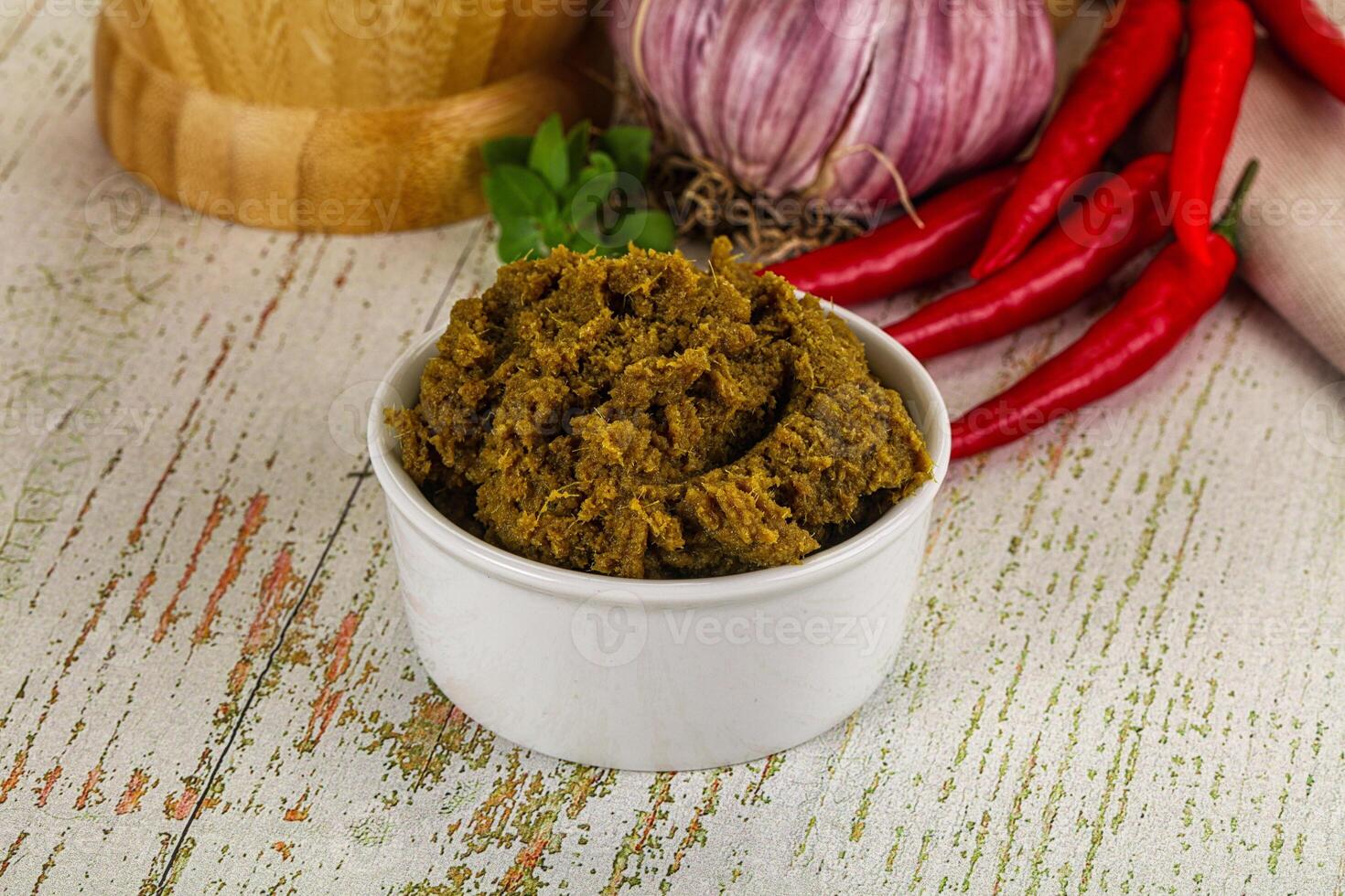 A bowl of green chili paste next to a pepper and a red onion photo