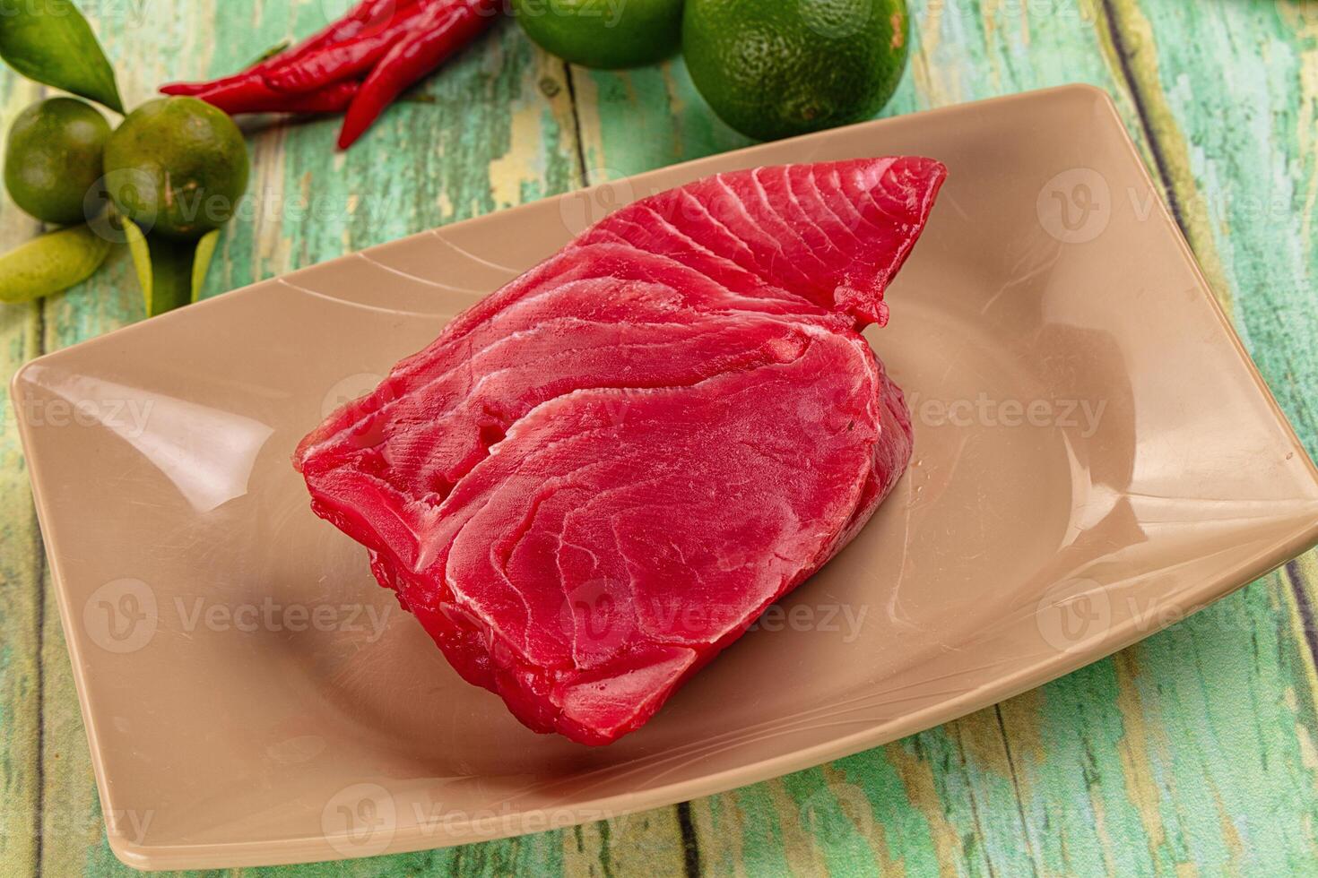 A piece of raw tuna on a plate with lime and green peppers photo