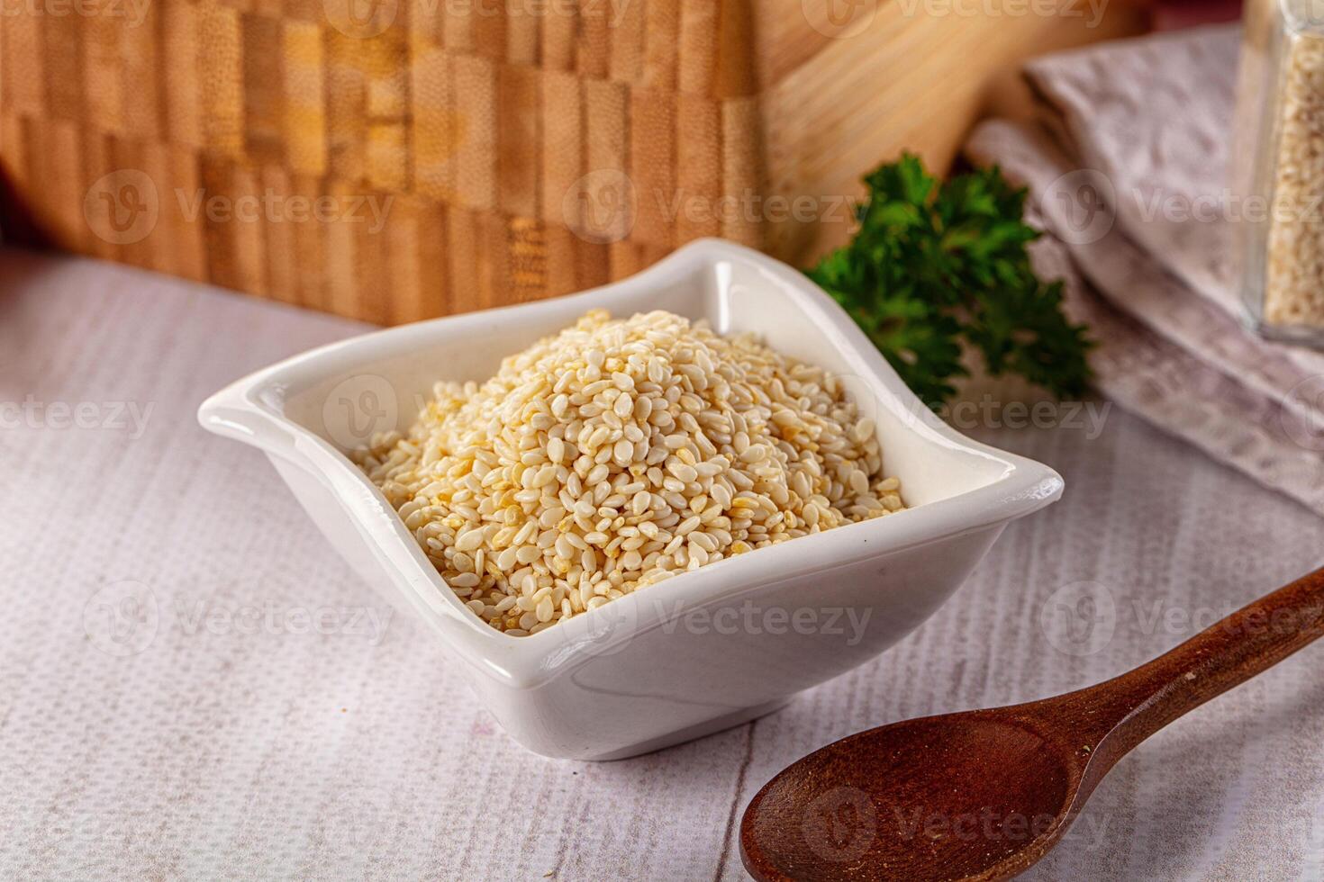 A bowl of sesame seeds and a wooden spoon on a table photo