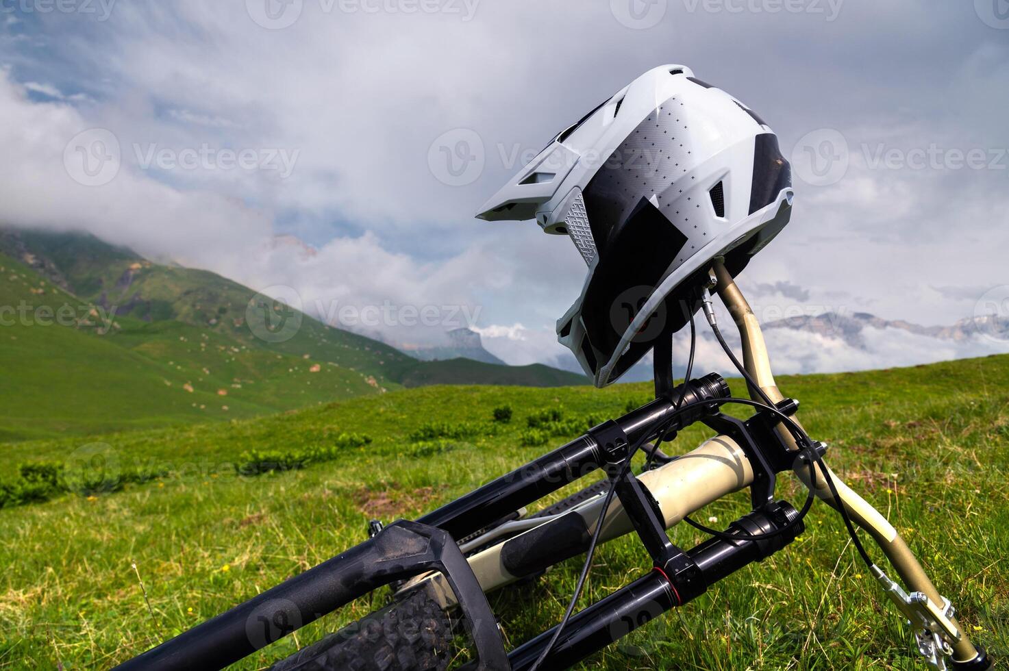 Black and white helmet and mountain bike. Off-road cycling gear. Off-road bike lying on grass in mountains photo