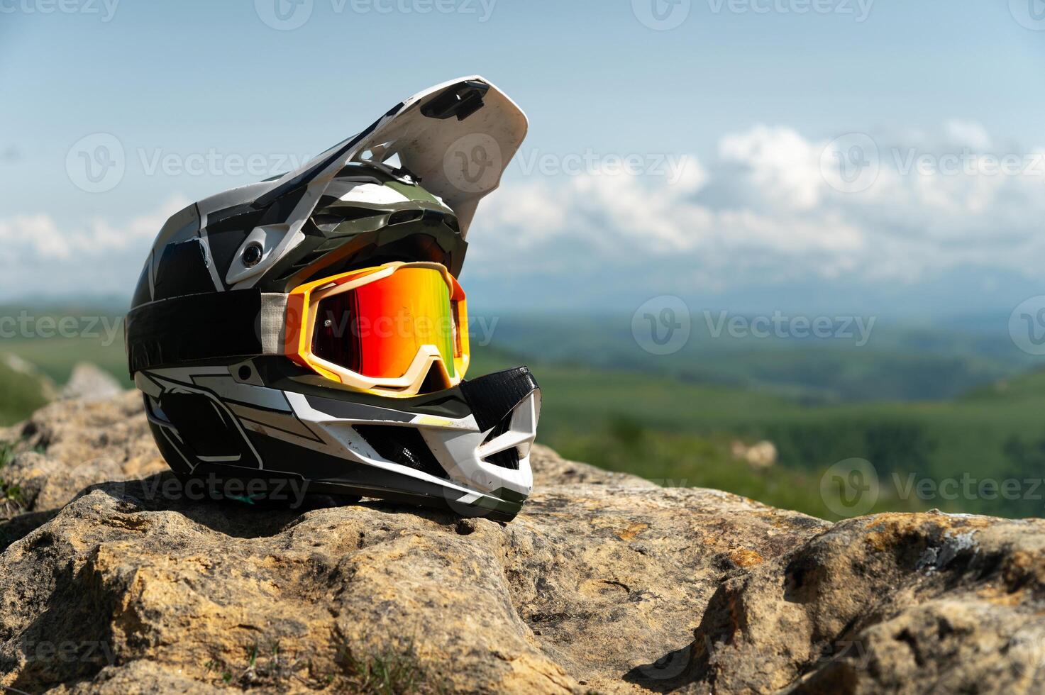 Side view of a full face black and white downhill mountain bike helmet. Extreme sports gear, against a backdrop of nature and a mountain landscape with cumulus clouds photo